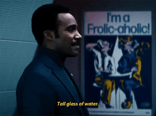 a man says tall glass of water in front of a poster that says i 'm a frolic-aholic