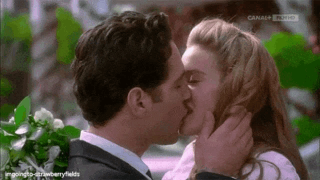 a man and a woman are kissing in front of a flower arrangement .