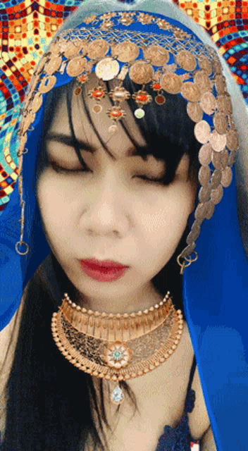 a woman with her eyes closed wearing a blue and gold headpiece and necklace
