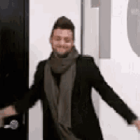 a man wearing a scarf and a black jacket is standing in front of a door .