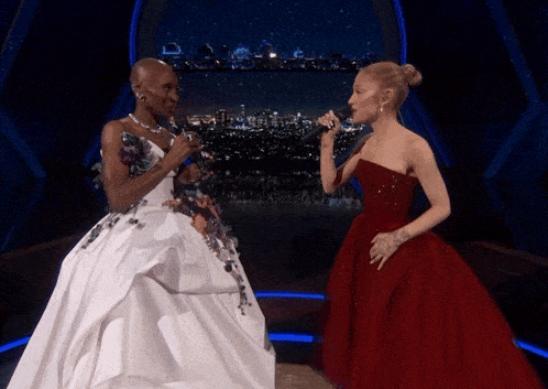 a woman in a white dress and a woman in a red dress singing into microphones