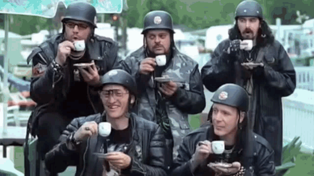 a group of men in motorcycle helmets are drinking coffee .
