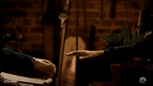 two men are holding hands in a dark room with the nbc logo in the background