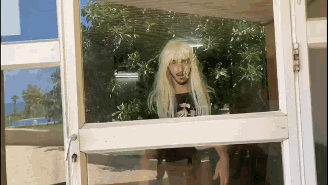 a man with blonde hair and a beard is standing in a doorway looking out the window .
