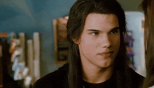 a young man with long hair is looking at the camera .
