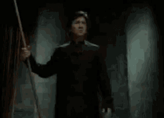 a man in a black robe is standing in a dark room holding a wooden stick .