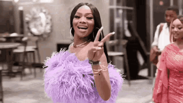 a woman in a purple dress is making a peace sign .