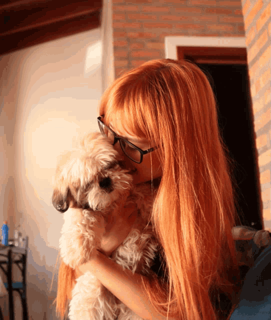 a woman with long red hair and glasses holds a small dog