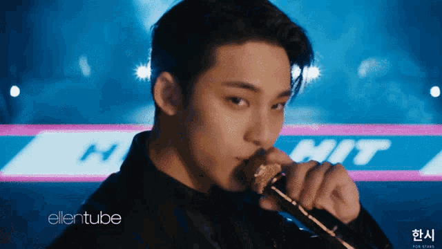 a close up of a man singing into a microphone with the ellentube logo behind him