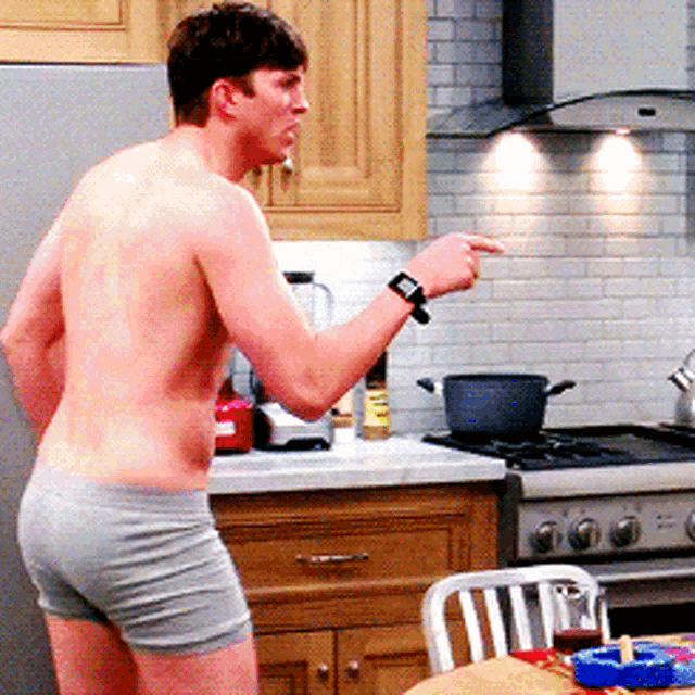 a shirtless man standing in a kitchen with a watch on his wrist
