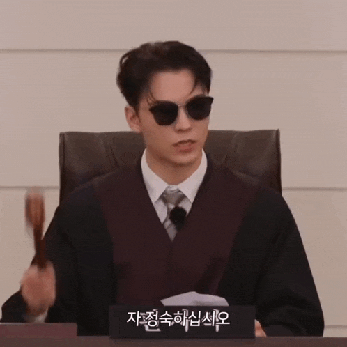 a man in a suit and tie is sitting at a table with a sign that says ' judge ' on it