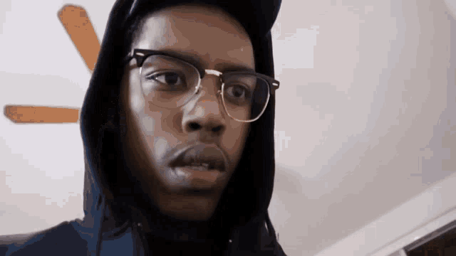a young man wearing glasses and a hooded jacket looks at the camera