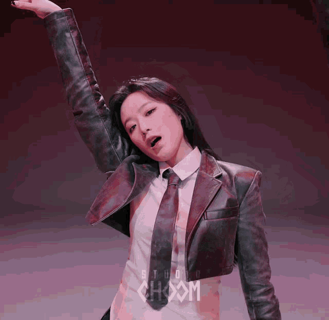 a woman in a leather jacket and tie is standing in front of a sign that says studio hoon