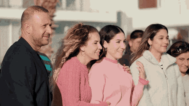 a group of people standing next to each other with one woman wearing a pink sweater