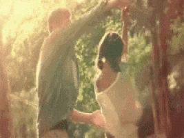 a man and a woman are dancing in a park with trees in the background .