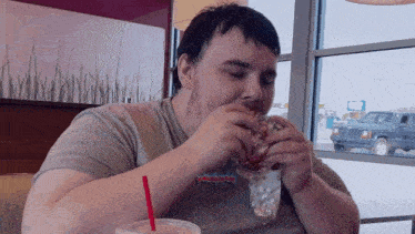 a man is eating a hamburger and drinking a milkshake in a restaurant