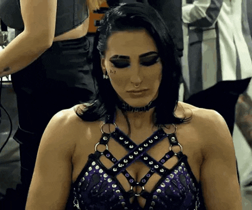 a woman in a purple top and choker is sitting down .