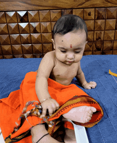 a baby is sitting on a bed with an orange blanket