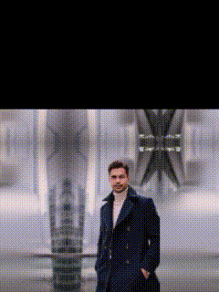 a man in a trench coat is standing with his hands in his pockets in front of a building .