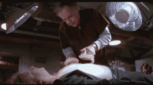 a man is laying on a table while a man in a lab coat holds a device over his chest
