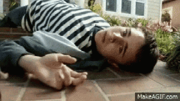 a young man in a striped shirt is laying on the ground with his hands on his chest .