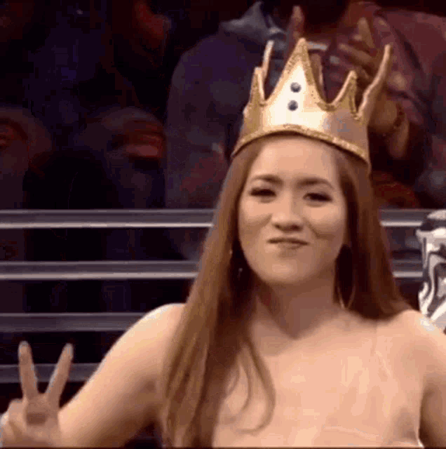 a woman wearing a crown on her head is giving a peace sign .