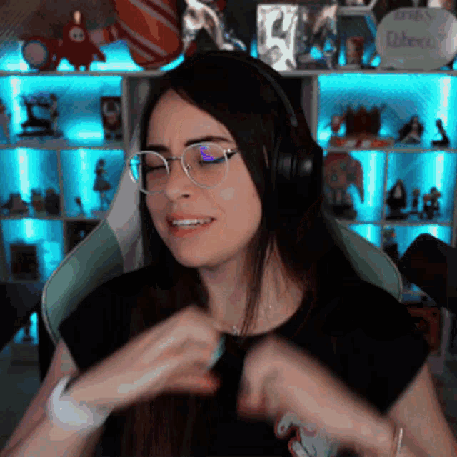 a woman wearing glasses and headphones is sitting in a chair in front of a shelf with toys on it .
