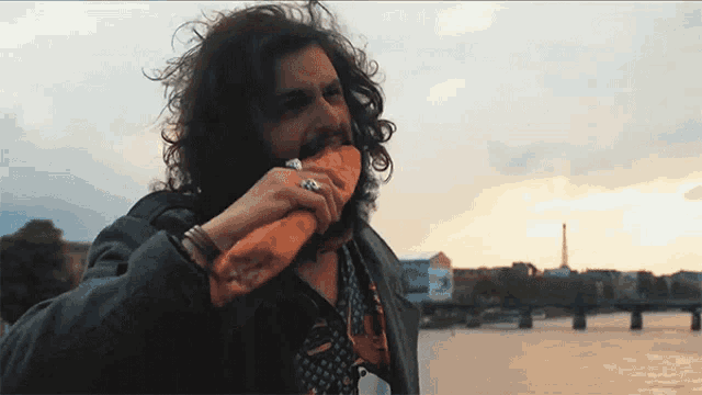 a man with long curly hair is eating a sandwich