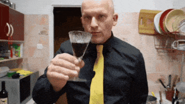 a man in a black shirt and yellow tie is holding a glass of wine