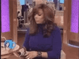 a woman in a blue sweater is sitting at a table with a cup of coffee in front of her .