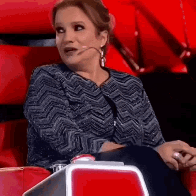 a woman is sitting in a red chair with a microphone in her mouth
