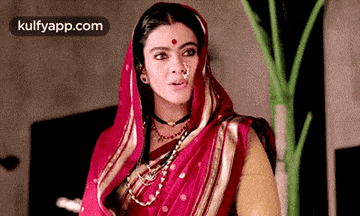 a woman wearing a red sari and a nose ring is standing in front of a plant .
