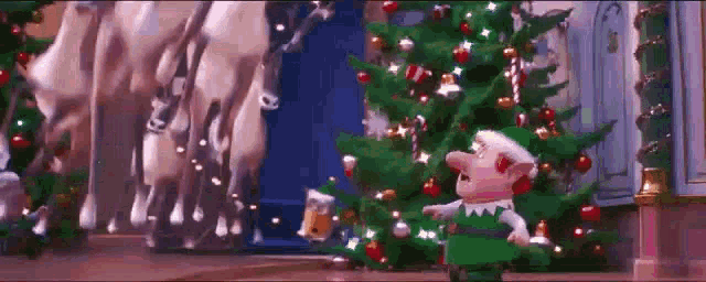 a christmas elf is standing in front of a christmas tree with reindeer behind him .