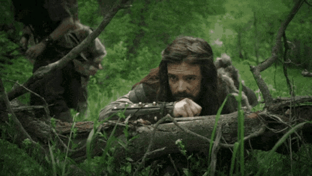 a man laying on a log in the woods with a gun in his hand