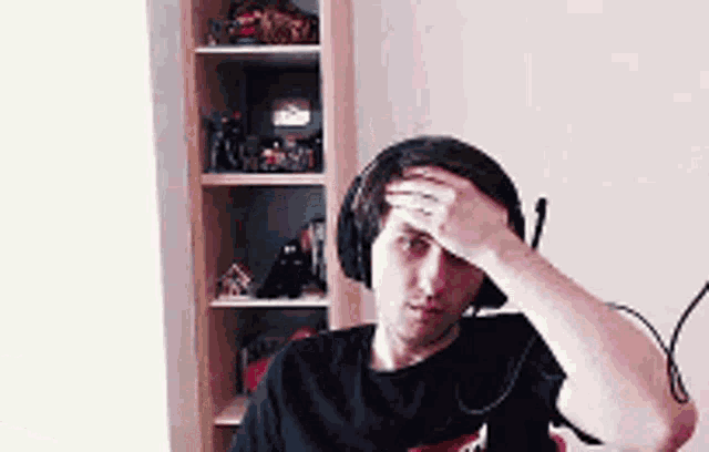 a man wearing headphones is scratching his forehead while sitting in front of a bookshelf .