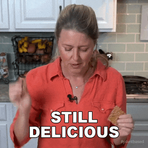 a woman in a red shirt says still delicious while eating a cracker