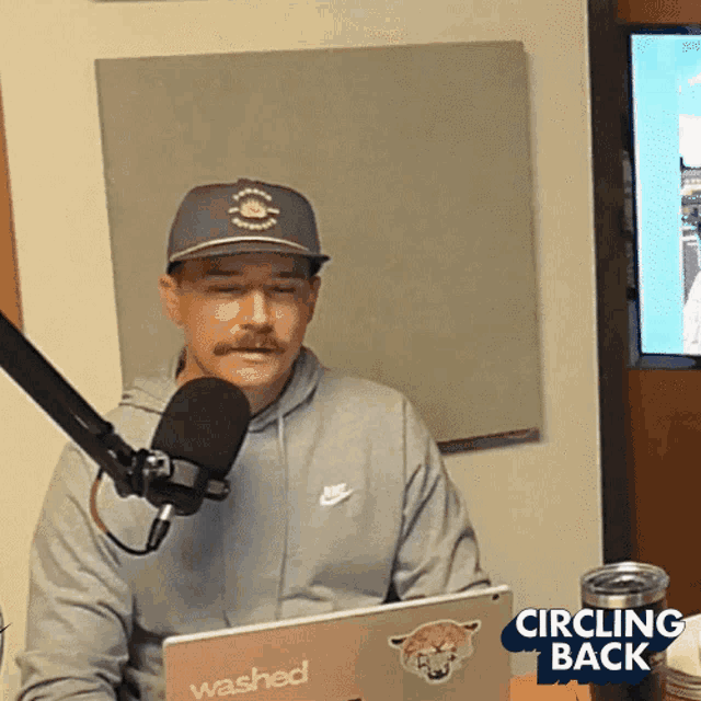 a man wearing a hat is sitting in front of a microphone and a laptop that says washed