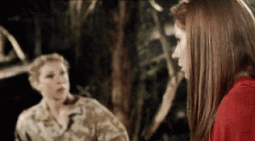 two women are standing next to each other in a forest .
