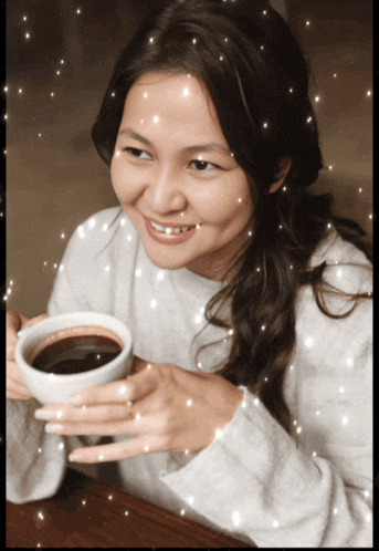 a woman in a white sweater is smiling and holding a cup of coffee