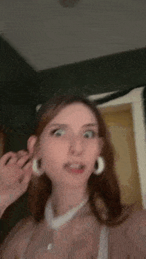 a woman with a nose ring and hoop earrings is standing in front of a mirror in a room .