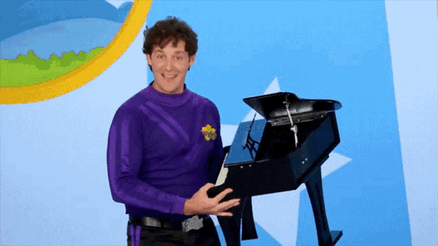 a man in a purple wiggle shirt holds a black piano