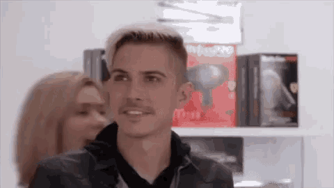 a man and woman are standing in front of a shelf with hair dryers on it .
