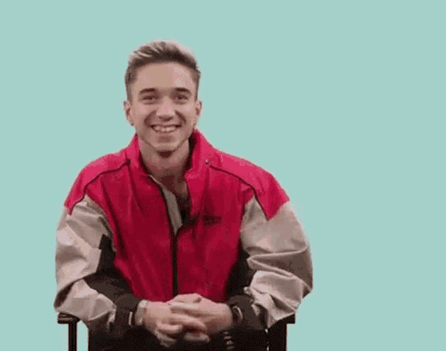 a young man wearing a red jacket is smiling and saying yeah .