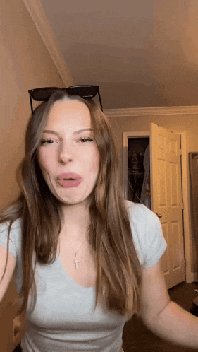 a woman wearing sunglasses and a cross necklace makes a face