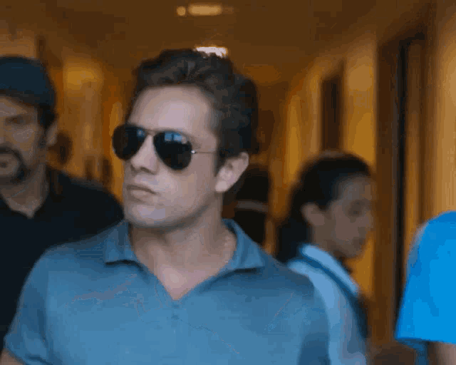 a man wearing sunglasses and a blue shirt is walking in a hallway