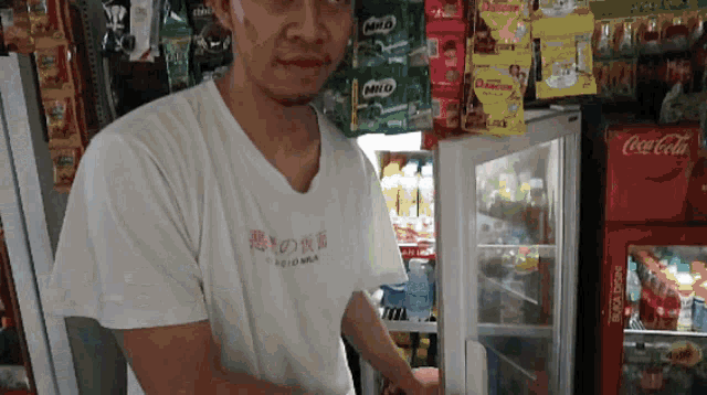 a man in a milo shirt stands in front of a coca cola cooler