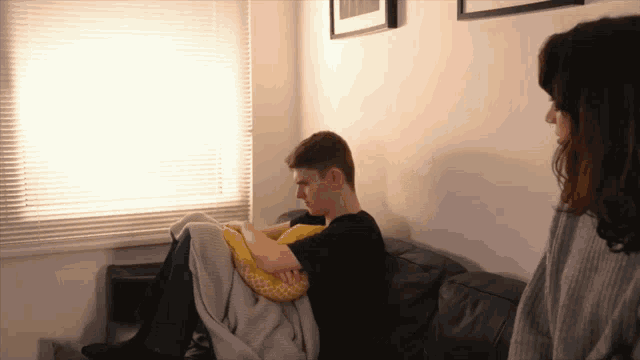 a man sits on a couch with a yellow pillow and a woman stands behind him