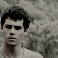a young man with a serious look on his face is standing in front of a bush .