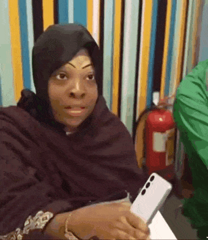 a woman wearing a hijab is holding a cell phone in her hand .