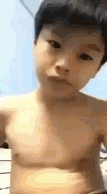 a young boy without a shirt is making a funny face while looking at the camera .